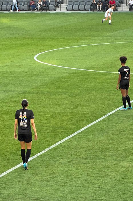 Christen Press and Simone Charley stand on the field in Pride jerseys during the ACFC vs Houston game.