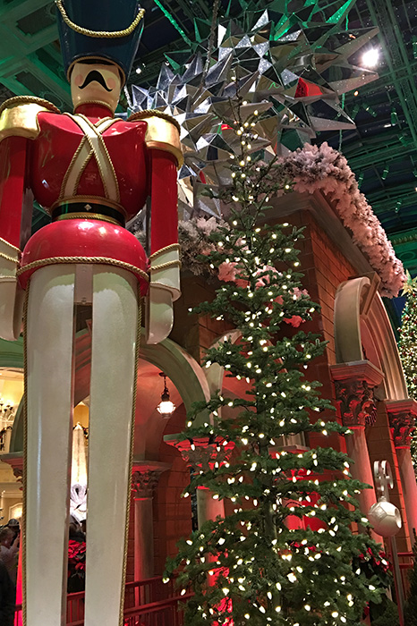 a giant toy soldier in red and cream uniform stands next to Christmas tree