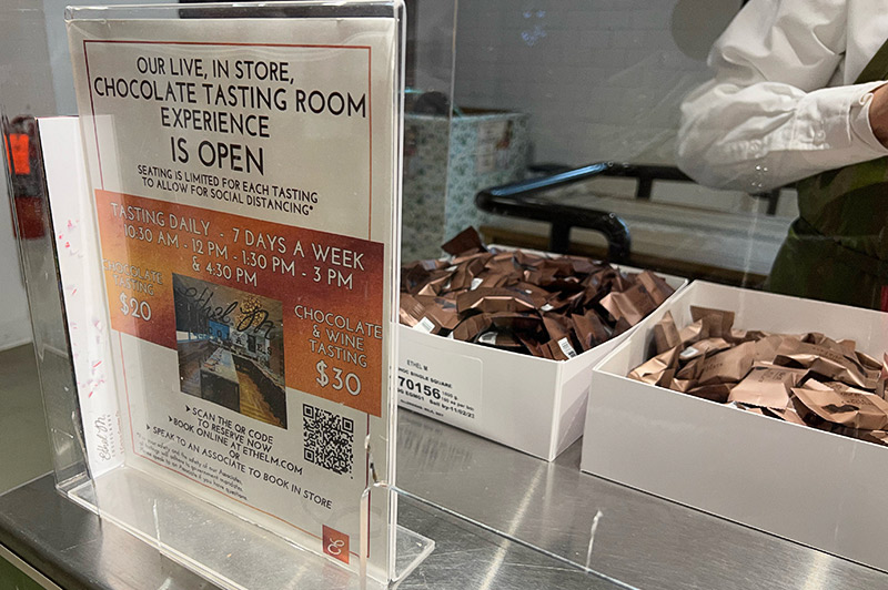 A sign for chocolate tastings sits in front of boxes of chocolate on a kiosk.