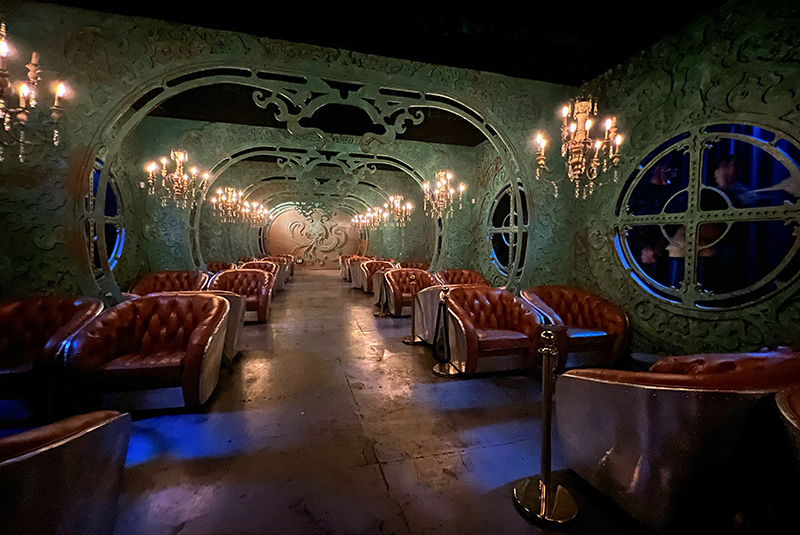 a room decorated as a submarine with plush leather seats, a carving of a giant squid in the background and portholes with moving fish with faces