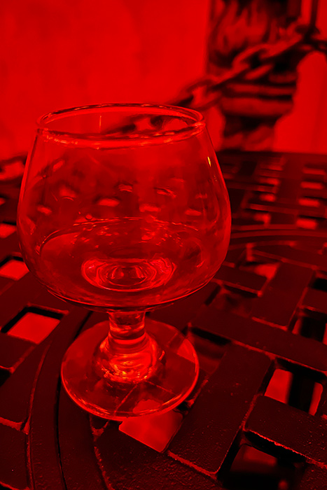 a glass of rum sits on a black metal table and glows red under red lights