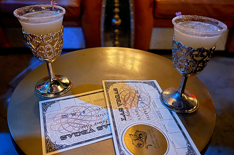 two cocktails in ornate silver cups sit with tasting cards on table in submarine section of Lost Spirits Distillery