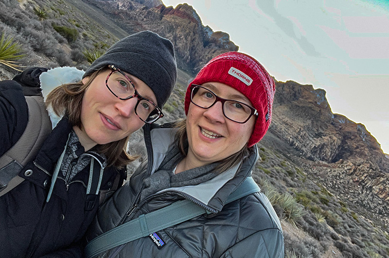 Shawna and Riley, dressed in warm hats and puffy coats, take a selfie in front of the mountains at Red Rock.