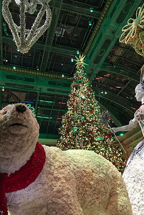 a polar bear and winter sorceress stand before giant Christmas tree with holiday chandelier hanging overhead